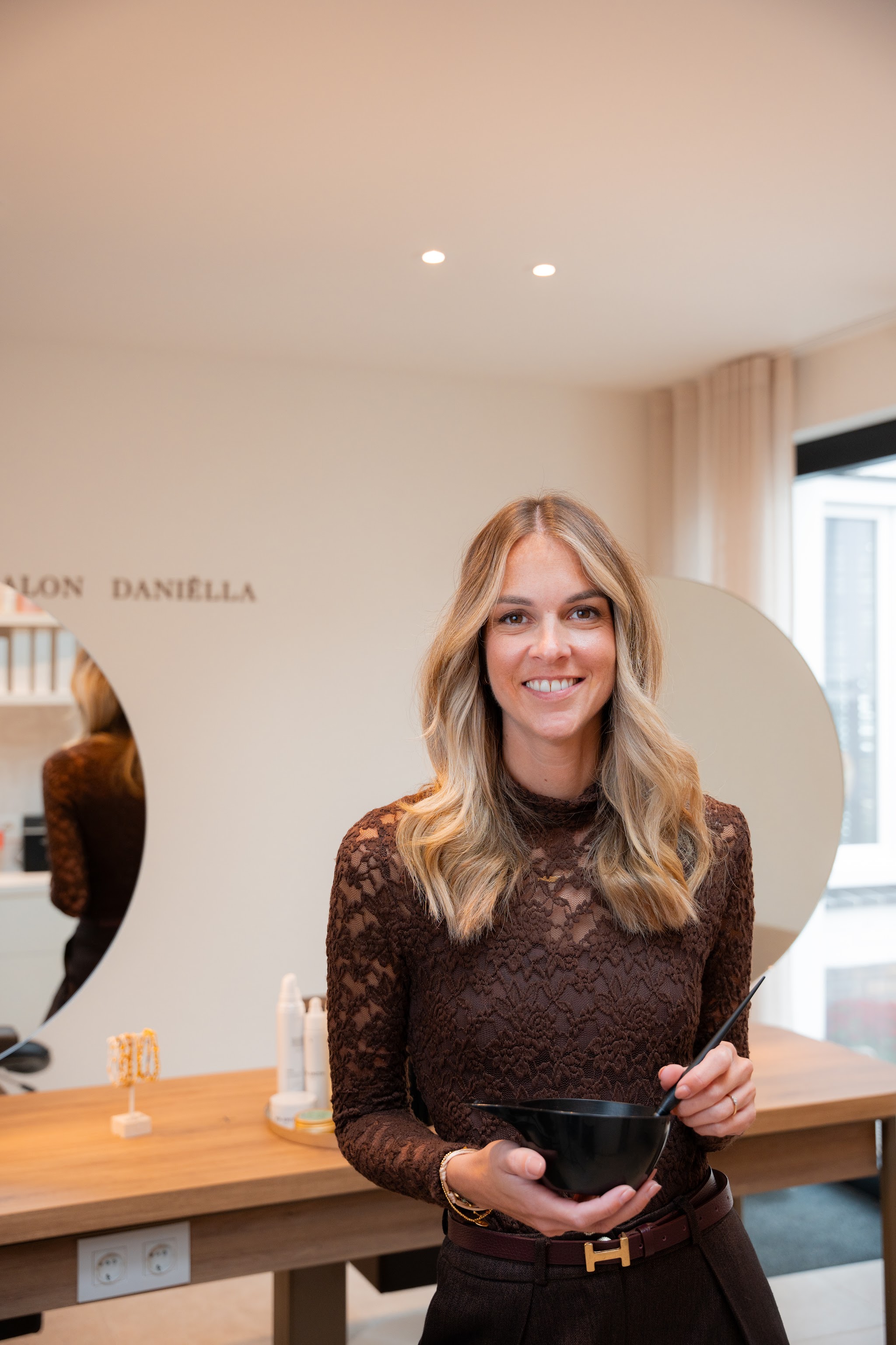 Kapster met een kleurkom aan de houten balie, met de letters van de salon op de muur